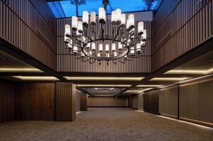 Un hall d’hôtel spacieux et moderne, agrémenté d’un grand lustre, de boiseries et d’un tapis à motifs.