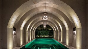 Un largo pasillo arqueado con una piscina central, columnas de piedra y un candelabro.