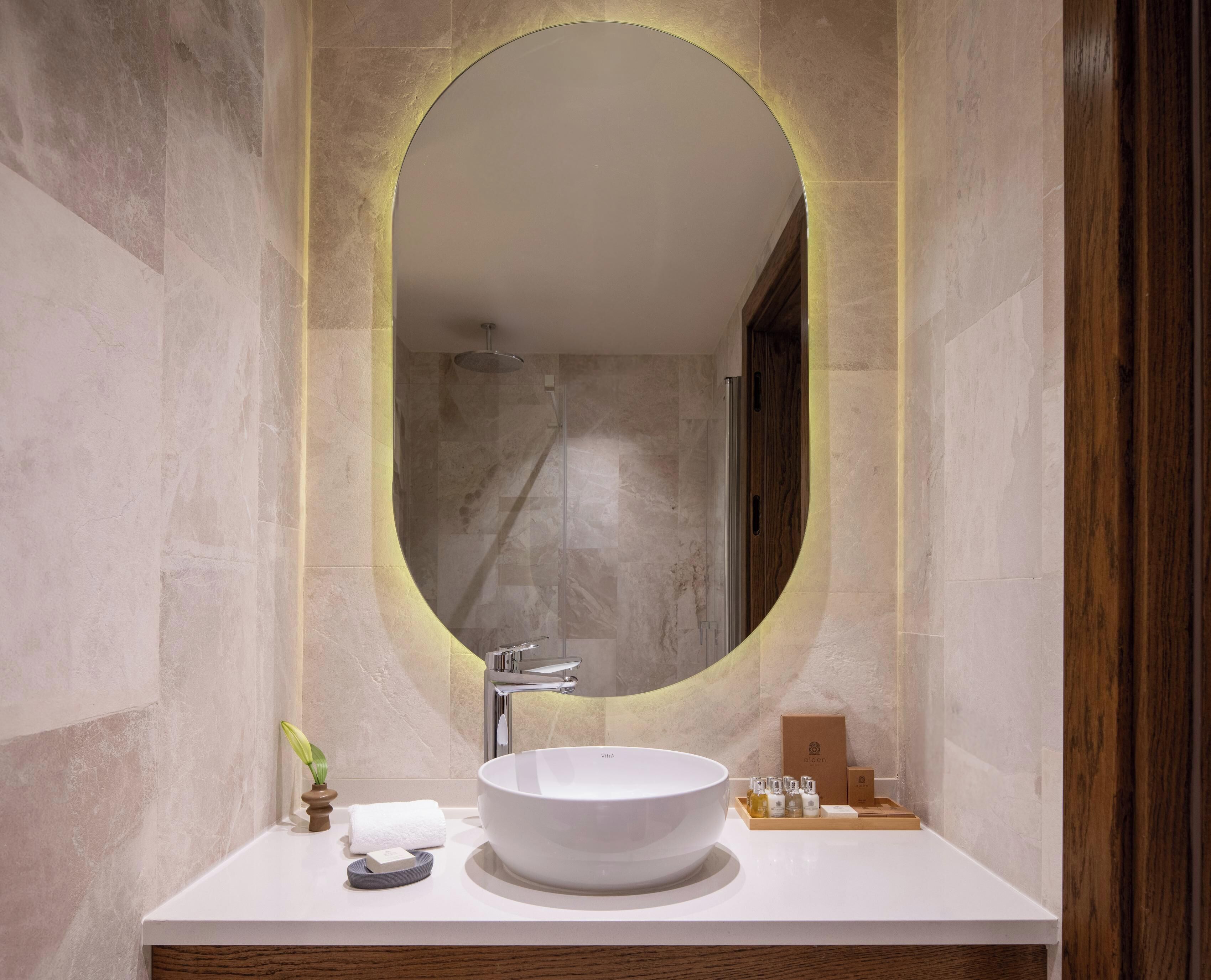 Un baño con un espejo ovalado grande, un lavabo blanco y un mueble de tocador de madera.