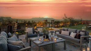 Un espacio de comedor al aire libre con suelo de piedra, un sofá y una mesa preparada para una comida, con vistas a un paisaje montañoso.