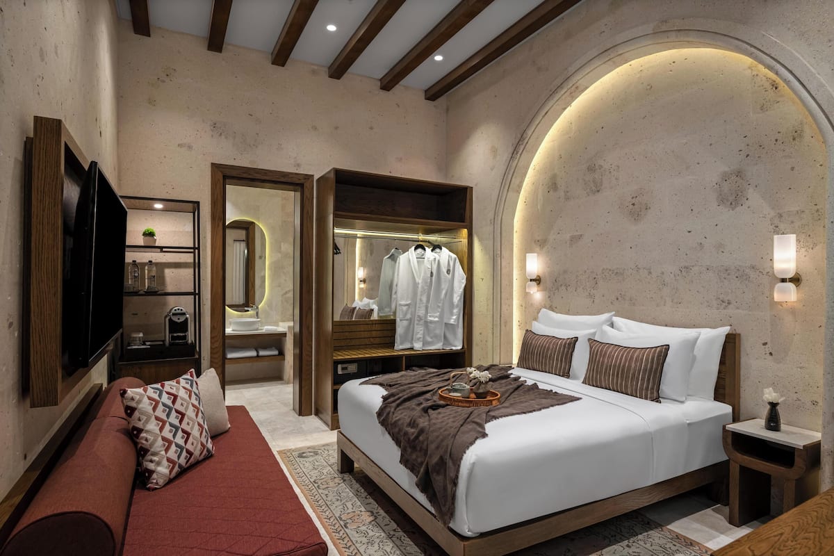 Un dormitorio con una cama grande, un banco de madera, un televisor, un armario y un espejo.