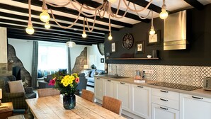 A modern kitchen with white cabinets, a wooden dining table, and a hanging light fixture. - Harbour Way - Seahouses  - sleeps 8 guests  in 4 bedrooms (Seahouses)