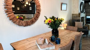 A dining area with a wooden table, wicker chairs, a mirror with a rustic frame, and a vase with flowers. - Harbour Way - Seahouses  - sleeps 8 guests  in 4 bedrooms (Seahouses)