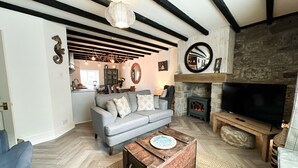 A cozy living room with a grey sofa, a wooden coffee table, a stone fireplace, and a television. - Harbour Way - Seahouses  - sleeps 8 guests  in 4 bedrooms (Seahouses)