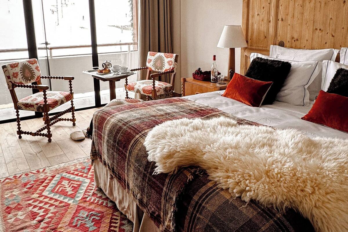 Ein Hotelzimmer mit einem großen Bett, einem Holzkopfbrett, einem Fenster mit Vorhängen, einem kleinen Tisch mit einer Lampe und zwei Stühlen.