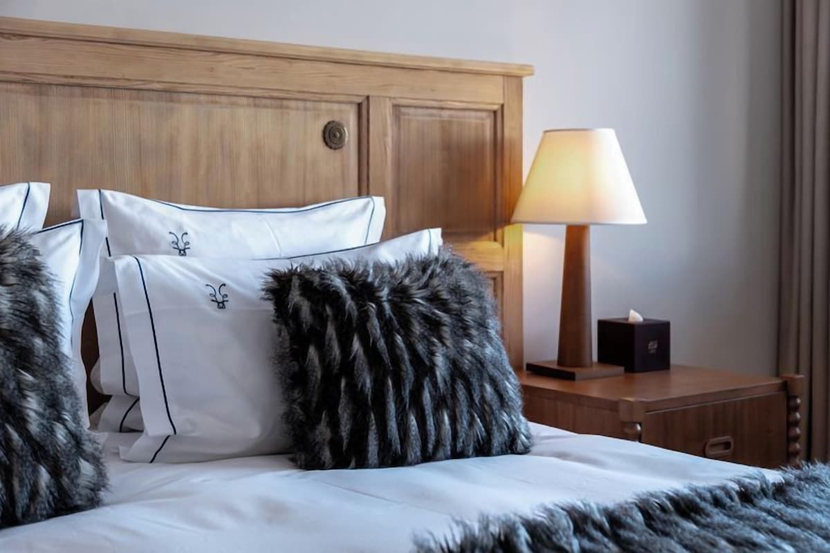 A neatly made bed with white linens and decorative pillows, a wooden headboard, and a bedside lamp.