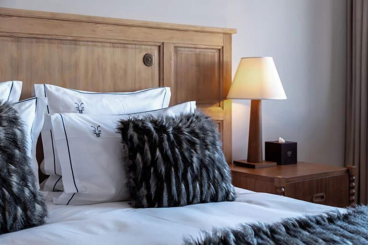 Ein ordentlich bezogenes Bett mit weißen Laken und Zierkissen, ein Holz-Kopfschild und eine Nachttischlampe.