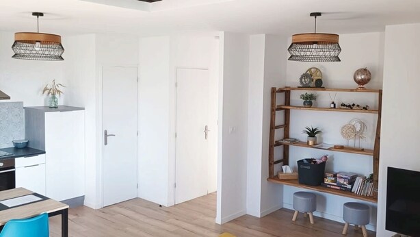 A spacious living area with a high ceiling, wooden beams, a sofa, a dining table with chairs, and a television. - Appartement Duplex Dans une Ancienne Usine (Beaupréau-en-Mauges)