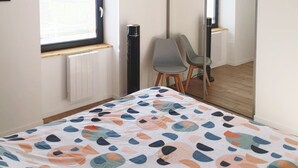 A bedroom with a bed, a window, a radiator, a mirror, and a chair. - Appartement Duplex Dans une Ancienne Usine (Beaupréau-en-Mauges)