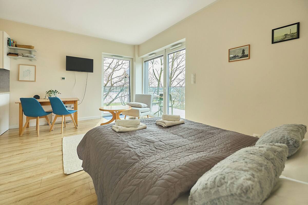 Quarto com cama grande, escrivaninha com cadeiras, televisão e varanda com vista.