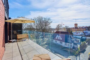 Ein Balkon mit Glasgeländer, einer Holzbank und einem gelben Sonnenschirm.