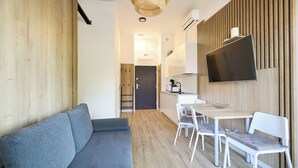 Ein stilvoller Wohnraum mit Sofa, Esstisch, Stühlen, einem Flachbildfernseher und einer Küchenzeile.