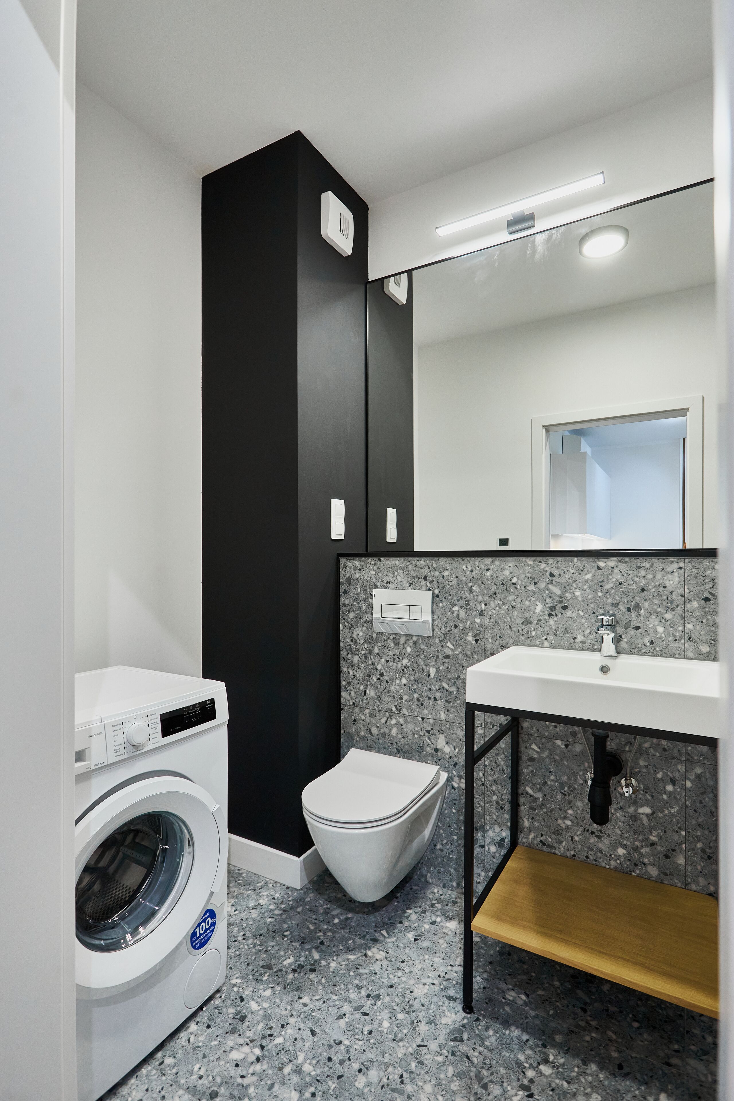 Une salle de bain moderne équipée d’un lave-linge, de toilettes, d’un lavabo et d’un miroir au-dessus du lavabo.