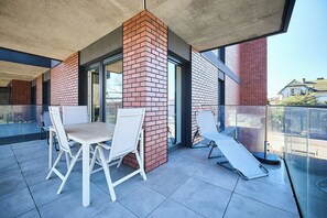 Ein Balkon mit Tisch und Stühlen, einer Glasreling und einer Backsteinmauer.