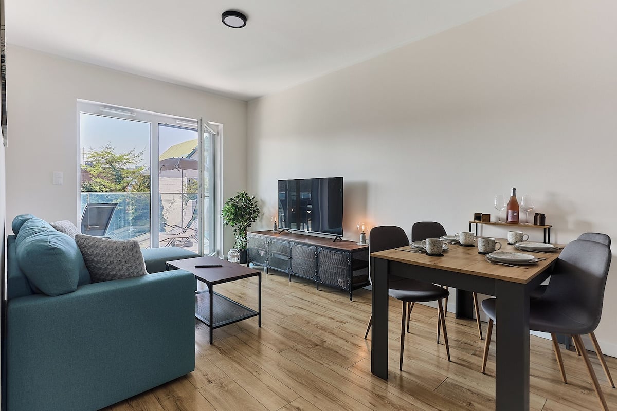 Uma sala de estar moderna com sofá, mesa de jantar, cadeiras, TV e uma porta de vidro deslizante que dá para uma área externa.