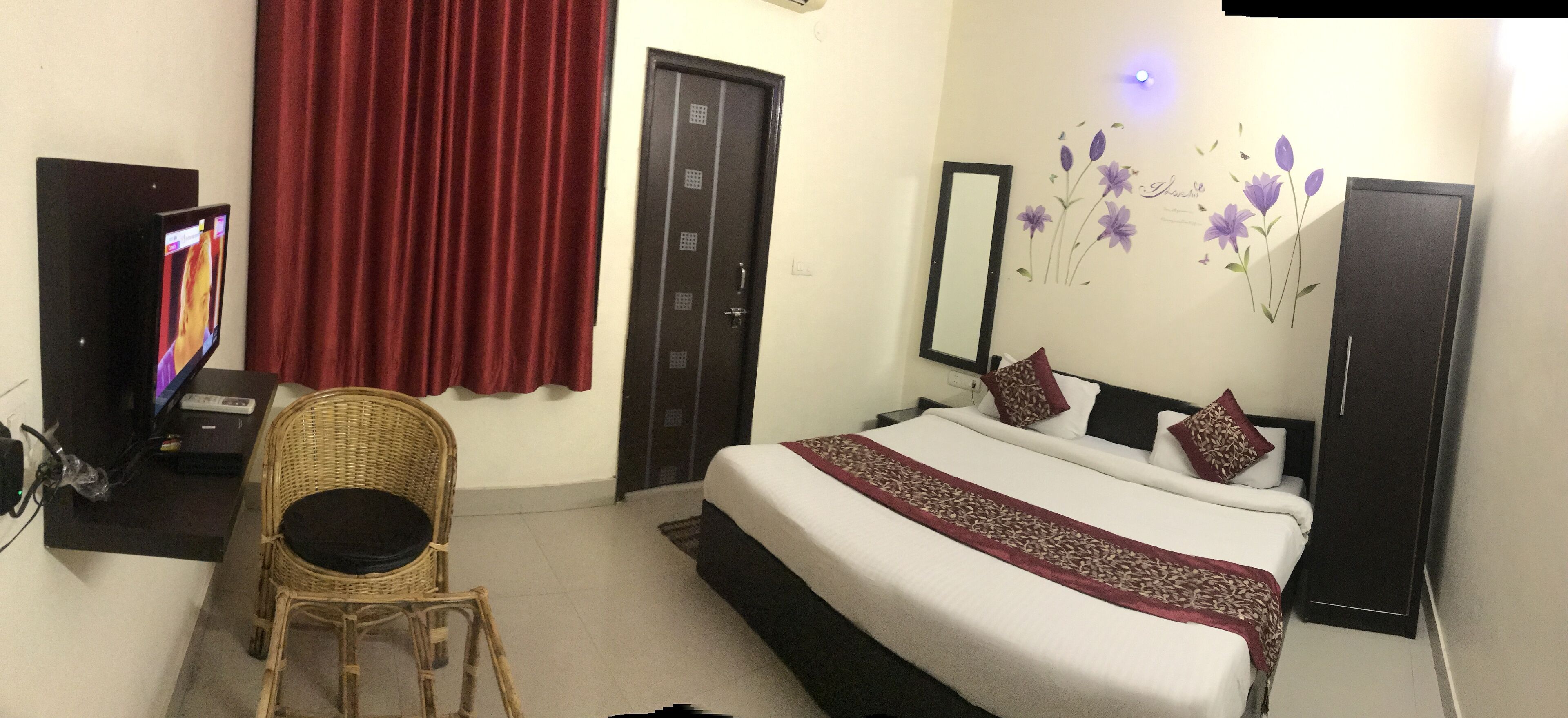 A hotel room with a bed, a television, a chair, a wardrobe, and a door.