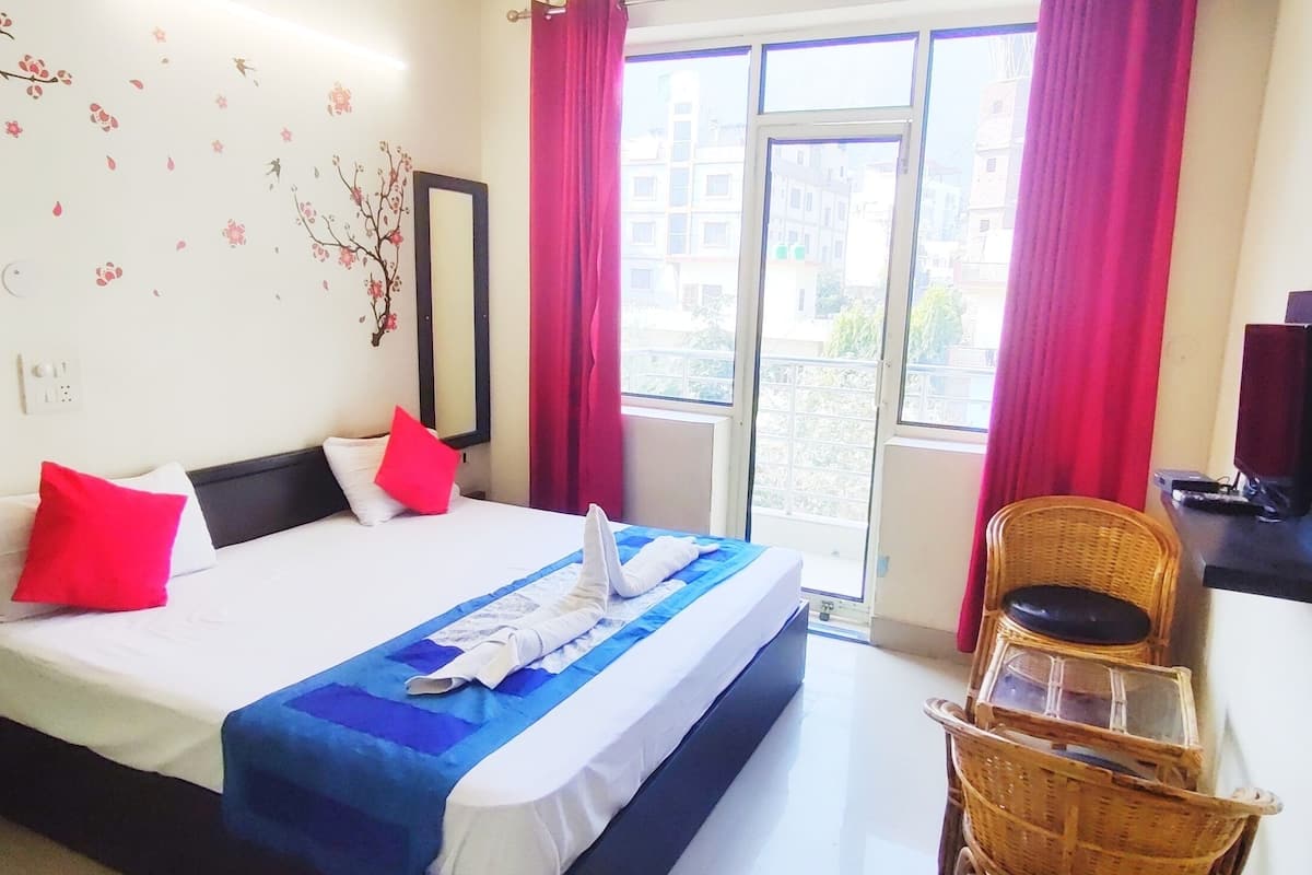 Une chambre d’hôtel équipée d’un lit, d’une télévision, d’une fenêtre avec des rideaux et d’un miroir fixé au mur.