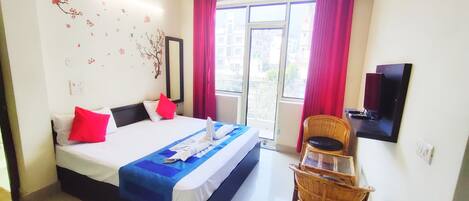A hotel room with a bed, a television, a window with curtains, and a wall-mounted mirror.