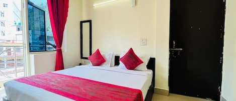 Ein Hotelzimmer mit einem großen Bett, roten Vorhängen, einer schwarzen Tür und Blick durch ein Fenster.