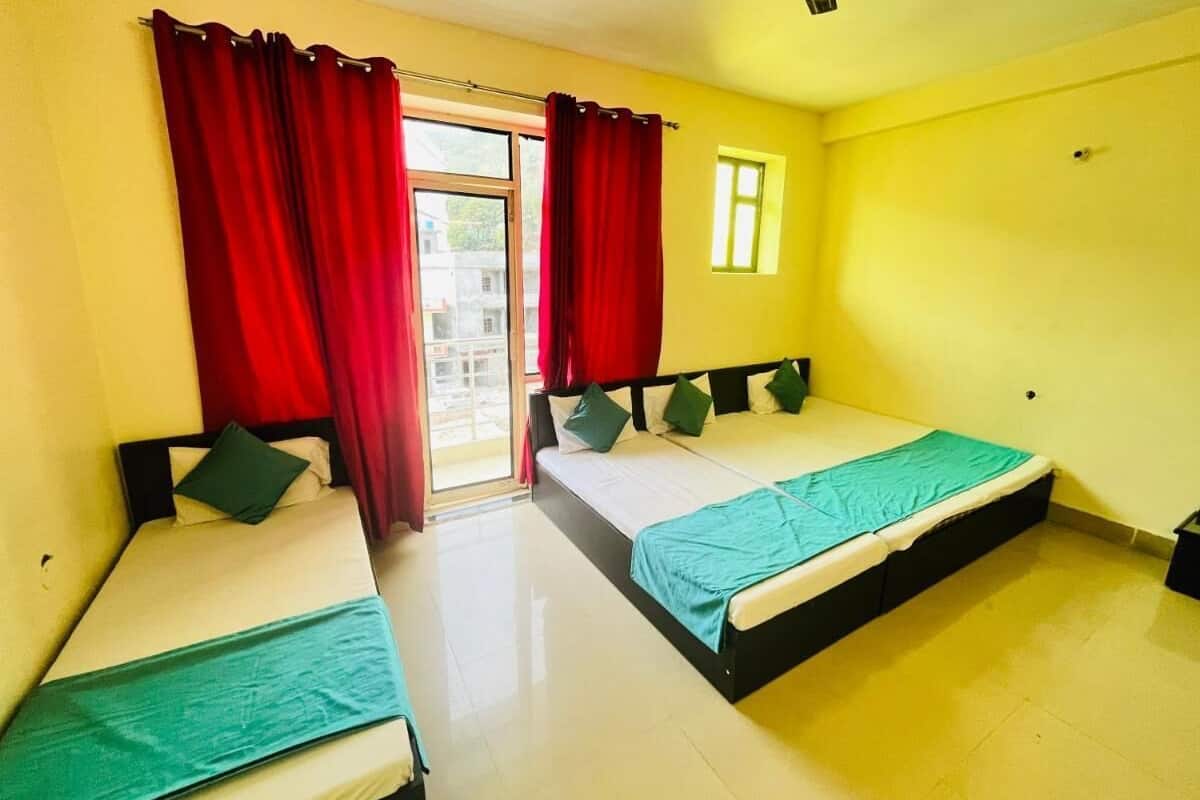 Une chambre avec deux lits simples, des rideaux rouges, une fenêtre et une petite table.