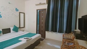 Ett hotellrum med en säng, en tv, ett fönster med gardiner och en väggdekoration.