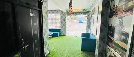 Un pasillo con alfombra verde artificial, un mostrador de recepción y un cartel en la pared.