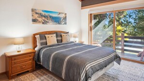 Une chambre avec un grand lit, des tables de chevet en bois, un tapis à motifs, un tableau au mur et une vue sur l’extérieur grâce à une porte coulissante.