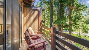 Une terrasse en bois avec un banc et des coussins, donnant sur une zone boisée.