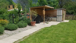Una rimessa in legno con una porta, una pianta in vaso e biciclette parcheggiate davanti.