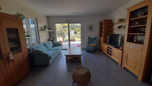 Un soggiorno con un divano, un tavolino, una televisione su un mobile in legno e un poggiapiedi in vimini.