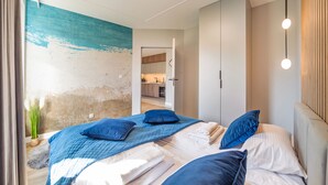 A bedroom with a bed, pillows, a nightstand, and a view into the kitchen.