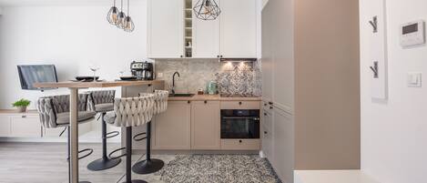 Una cocina moderna con comedor, que incluye una isla de cocina, taburetes de bar, iluminación colgante y un horno empotrado.
