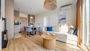 A modern living room with a wooden floor, a round coffee table, a white sofa with blue and beige cushions, and a dining area with a table and chairs.