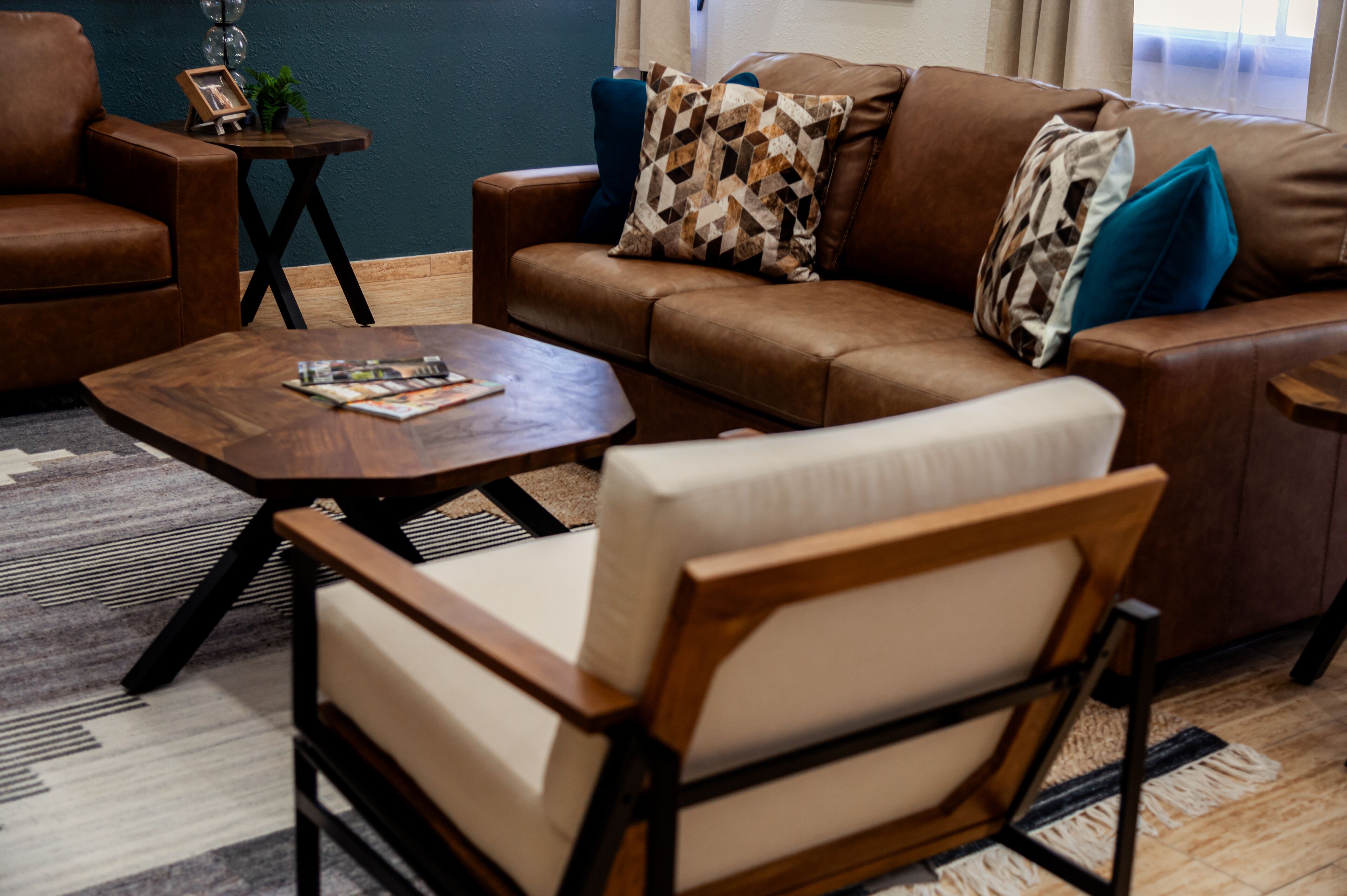 Een woonkamer met een bruine leren bank, een houten salontafel en een beige fauteuil.