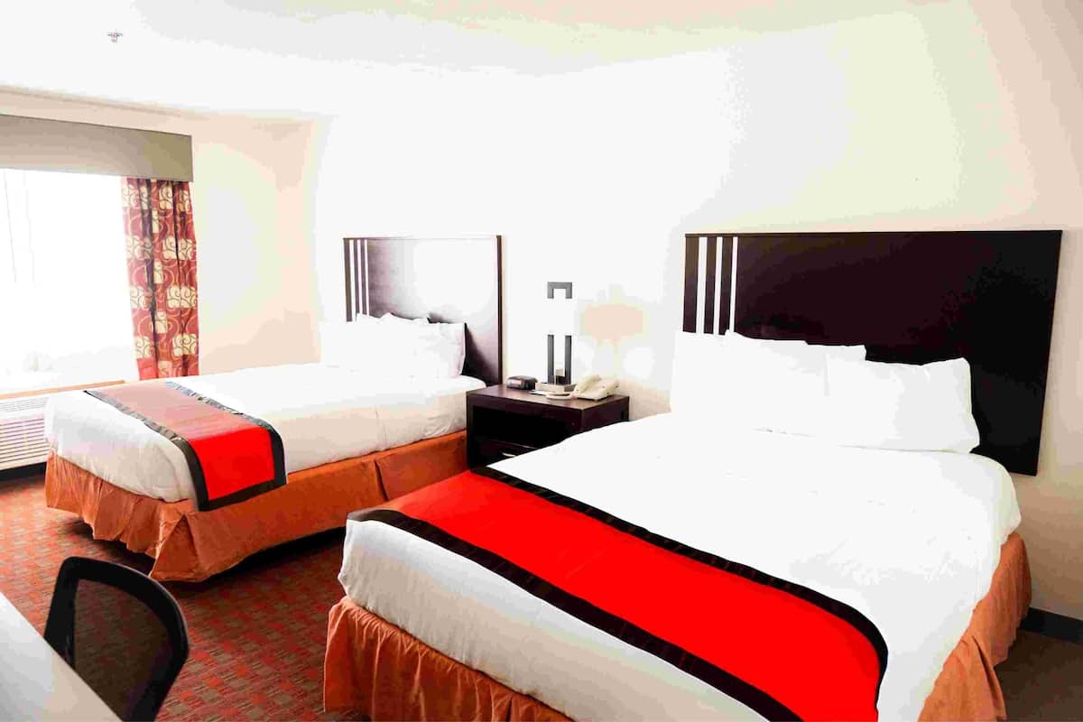 Een hotelkamer met twee bedden, een nachtkastje, een lamp en een raam met gordijnen.