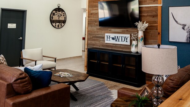 A modern living room with a wooden accent wall, a mounted TV, and a chandelier. - OK Welcome Home Hotel (Alva)