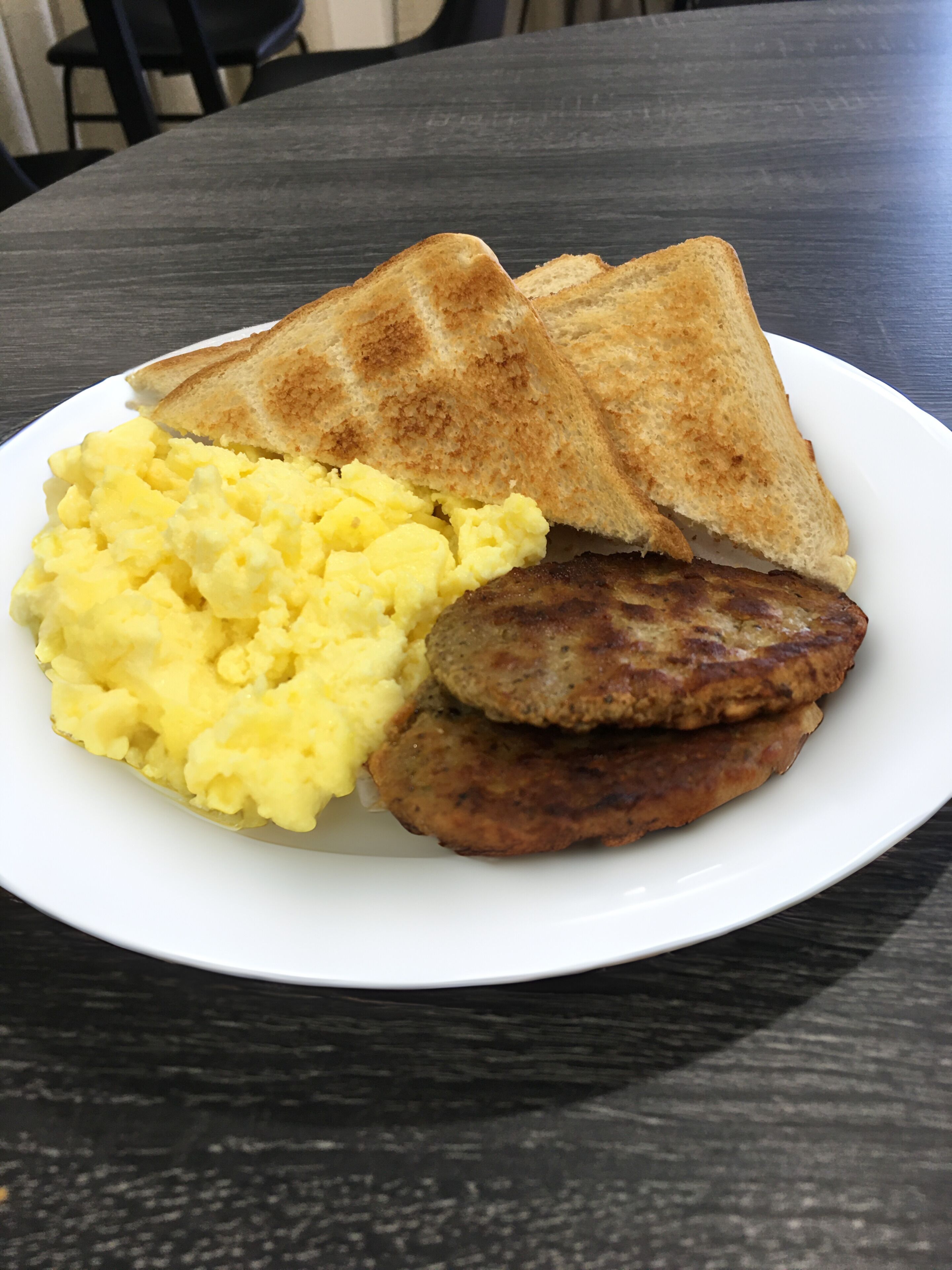 A plate with scrambled eggs, toast, and a sausage patty.