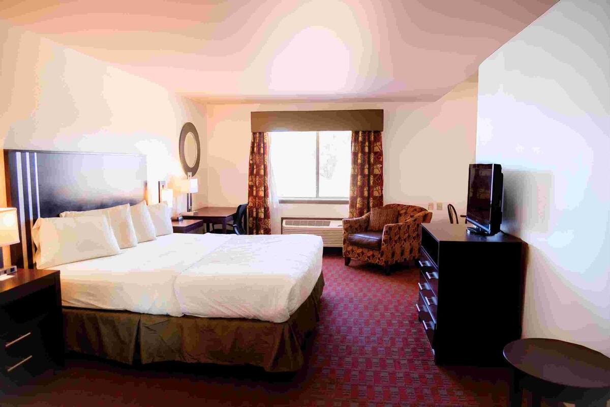 Een hotelkamer met een groot bed, een bureau met lamp, een stoel, een televisie en een raam met gordijnen.