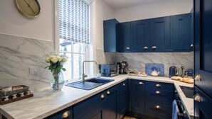 Una cucina moderna con mobili scuri blu, un piano di lavoro in marmo e una sveglia appesa al muro.