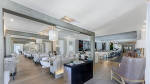 Un hall d’hôtel spacieux et moderne, doté d’un comptoir d’accueil central, de plusieurs espaces salon et d’une grande fenêtre offrant une vue sur l’intérieur.