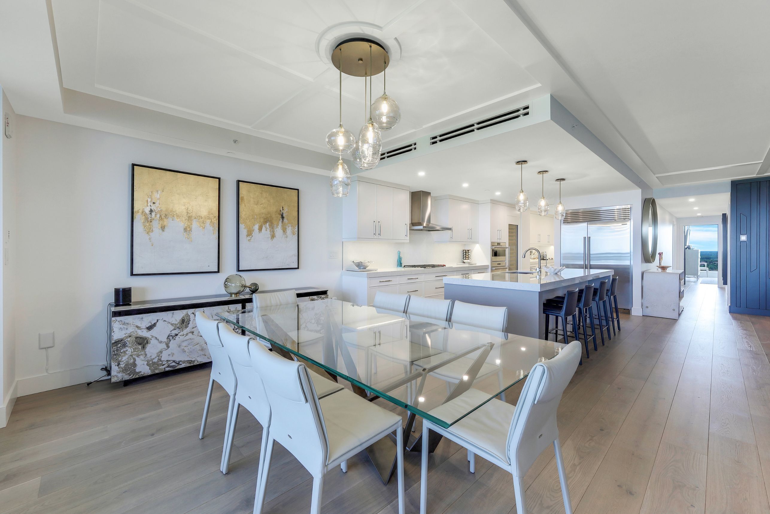 Una cocina moderna con muebles blancos, una mesa de comedor de vidrio e iluminación colgante.