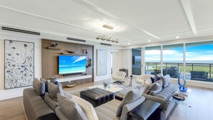 Un salon moderne doté d’un grand téléviseur à écran plat, de sièges confortables et offrant une vue sur le paysage grâce à de grandes fenêtres.