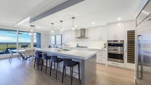 Une cuisine moderne dotée d’un grand îlot central, d’appareils électroménagers en acier inoxydable et offrant une vue sur l’extérieur.