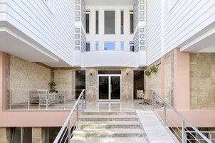 A modern building with a central staircase, a glass door entrance, and a balcony with outdoor seating.