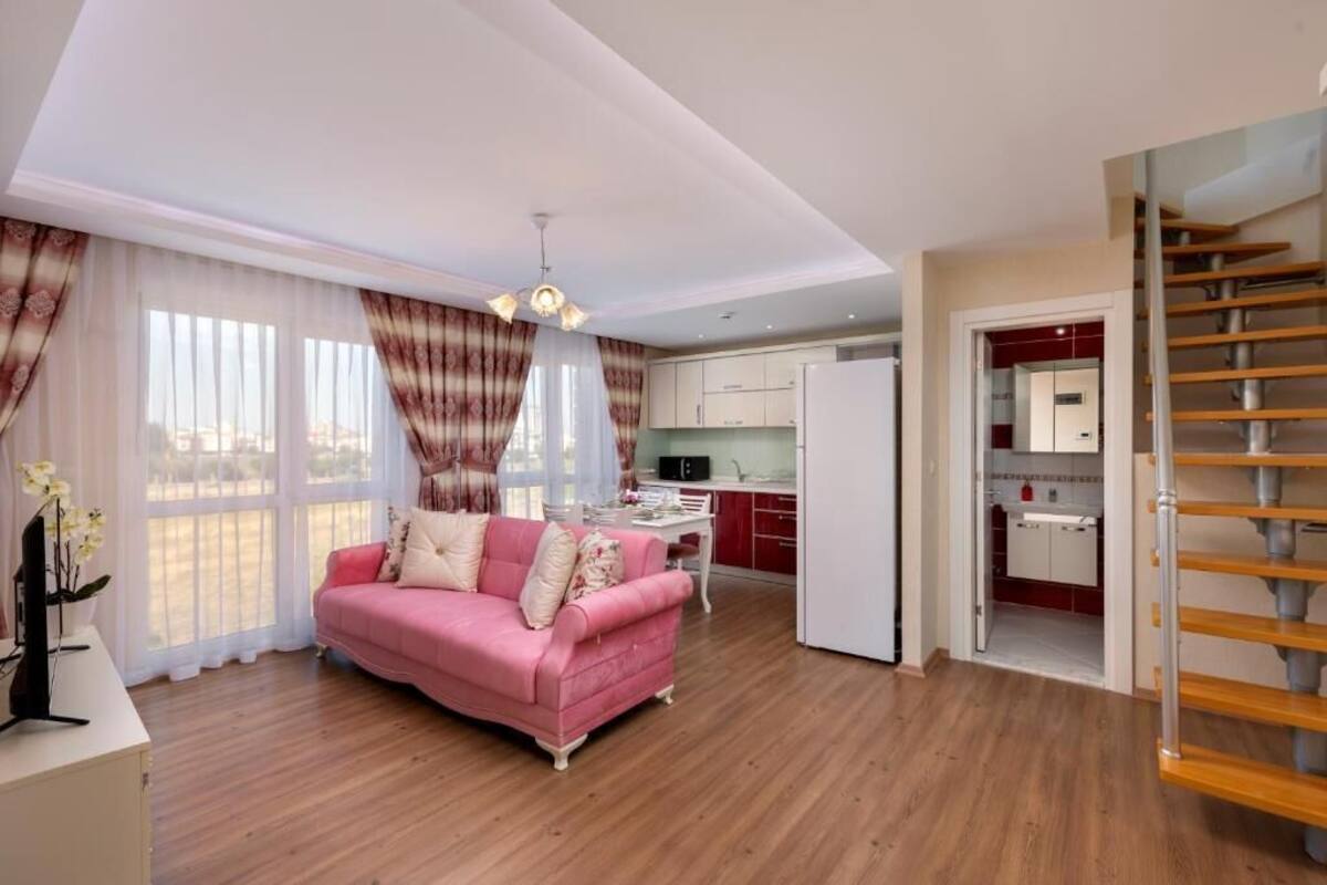 A modern living room with a pink sofa, a dining area, and a kitchen.