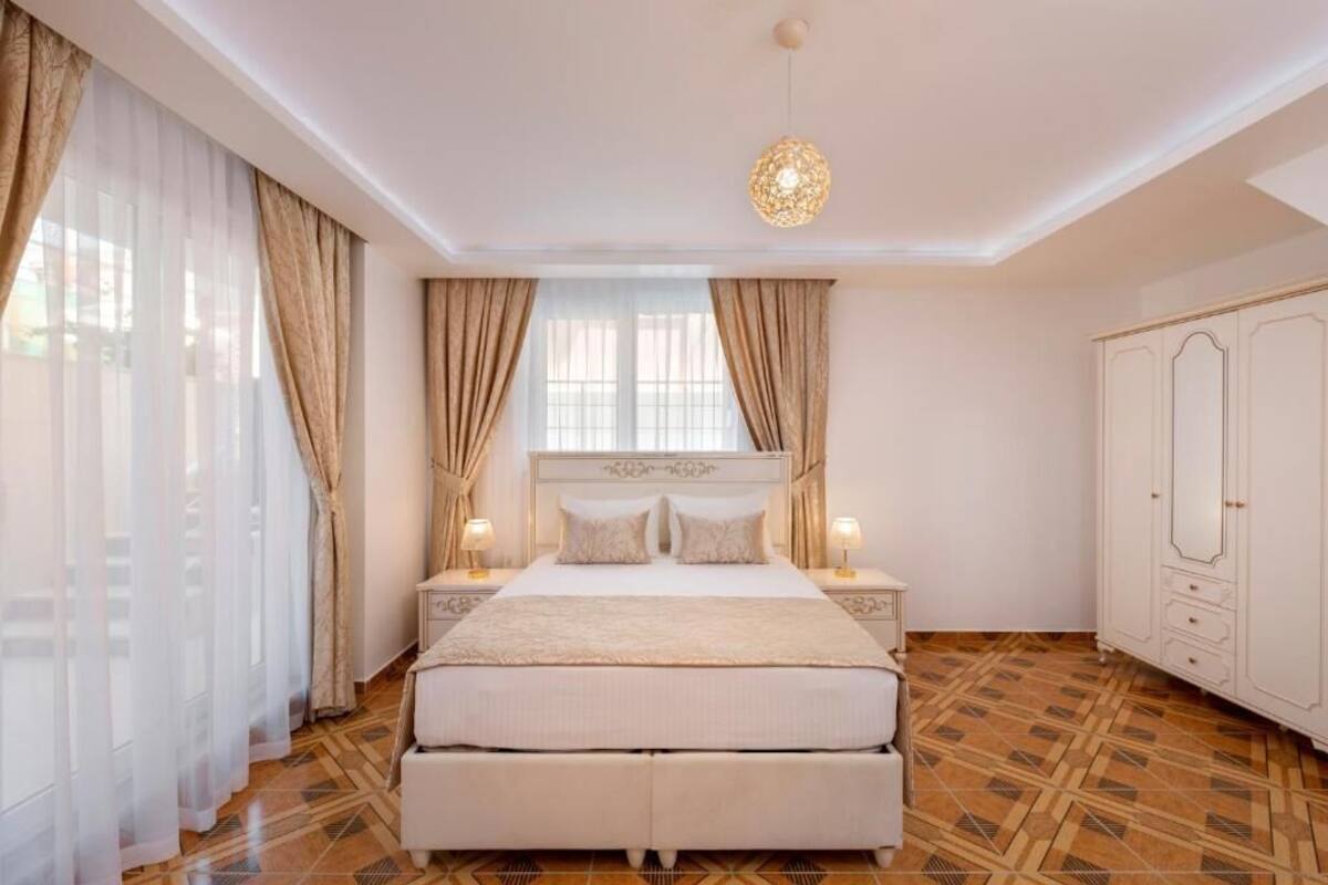 A bedroom with a large bed, two bedside tables with lamps, a wardrobe, and a patterned floor.