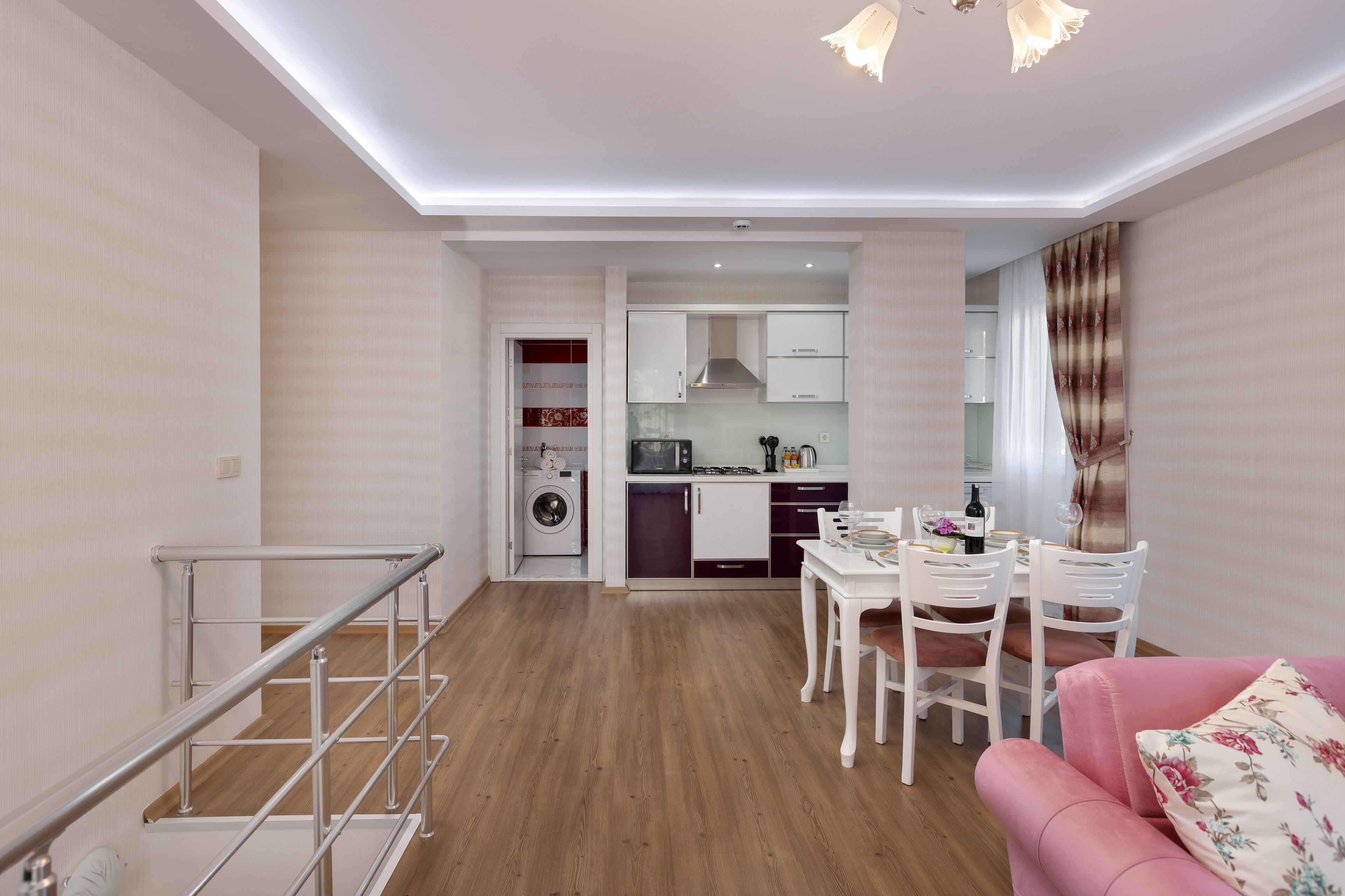 Una cocina moderna con armarios blancos y un comedor con un sofá rosa y sillas blancas.