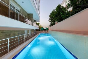 A swimming pool with a tiled edge, a metal railing, and a view of a building with a balcony. - Onix Apart Hotel (Konyaalti)