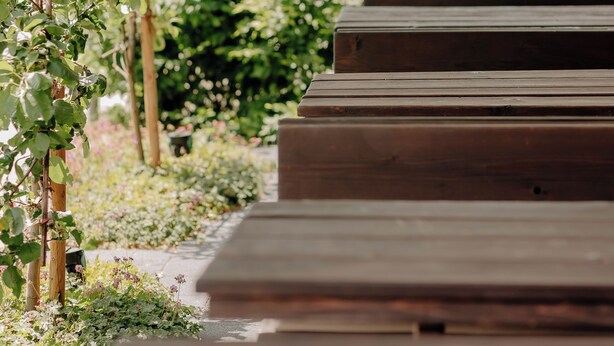 A covered outdoor seating area with wooden benches and a row of green plants. - INSIDE Nordhorn by Hackmann (Nordhorn)