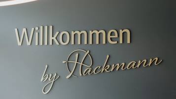 Letrero de bienvenida con el texto 'Willkommen by Rackmann' sobre una pared gris.